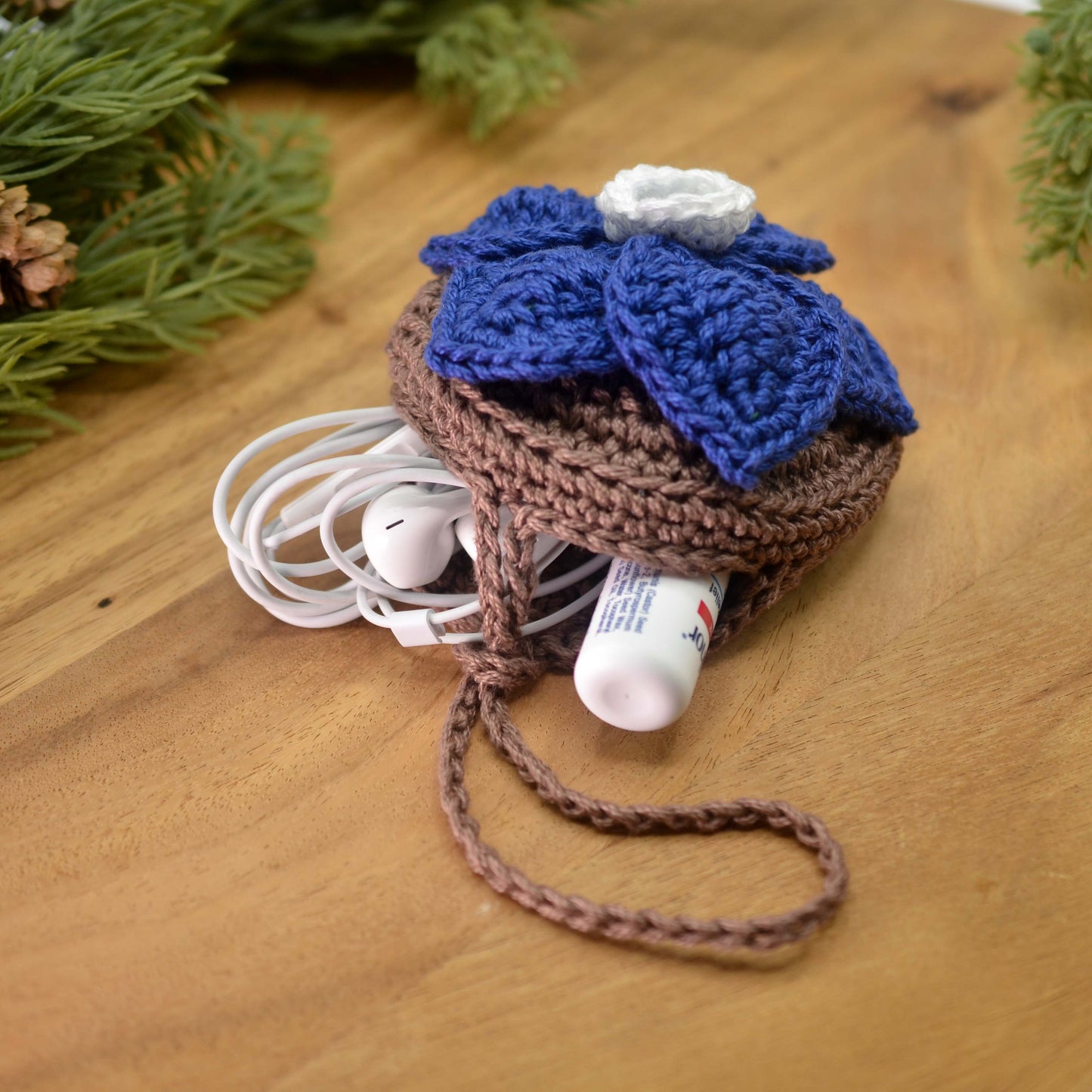 Crocheted blue floral pouch with earphone and lip balm stored in it.