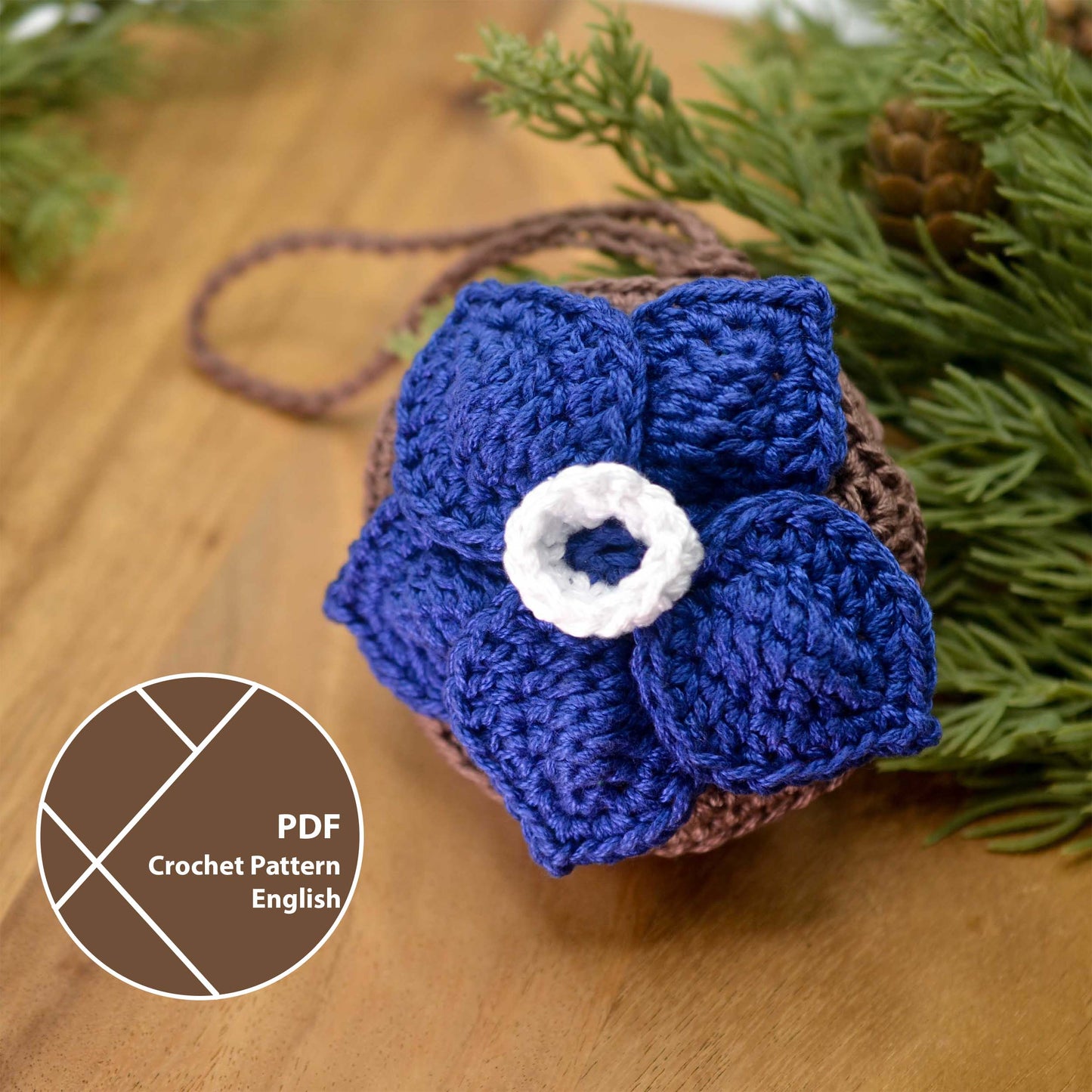 Crocheted blue flower pouch displayed on the desktop with green branches on the background.
