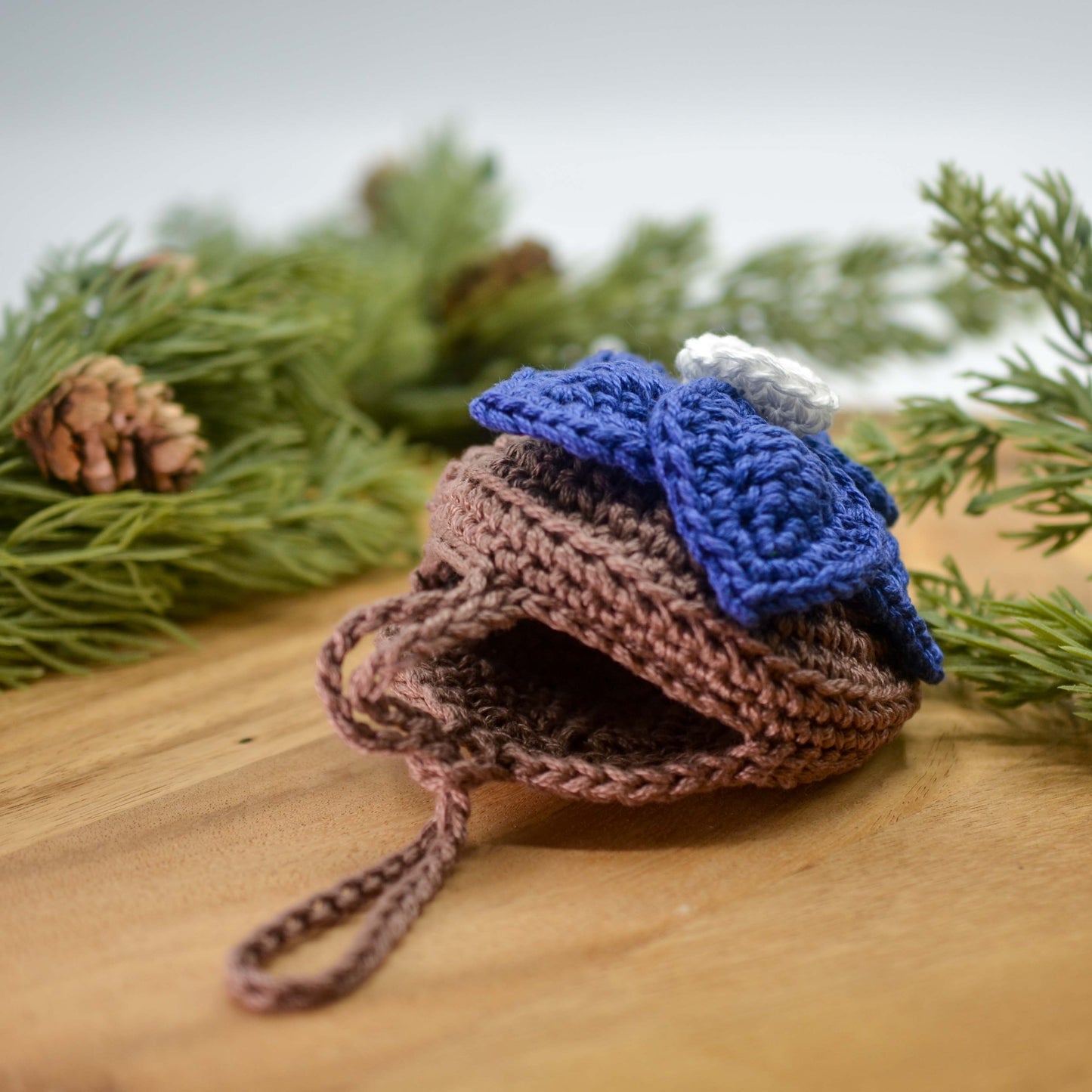 Crocheted floral pouch lying on the desktop against a greenery background. The pouch is half open, and it's empty.
