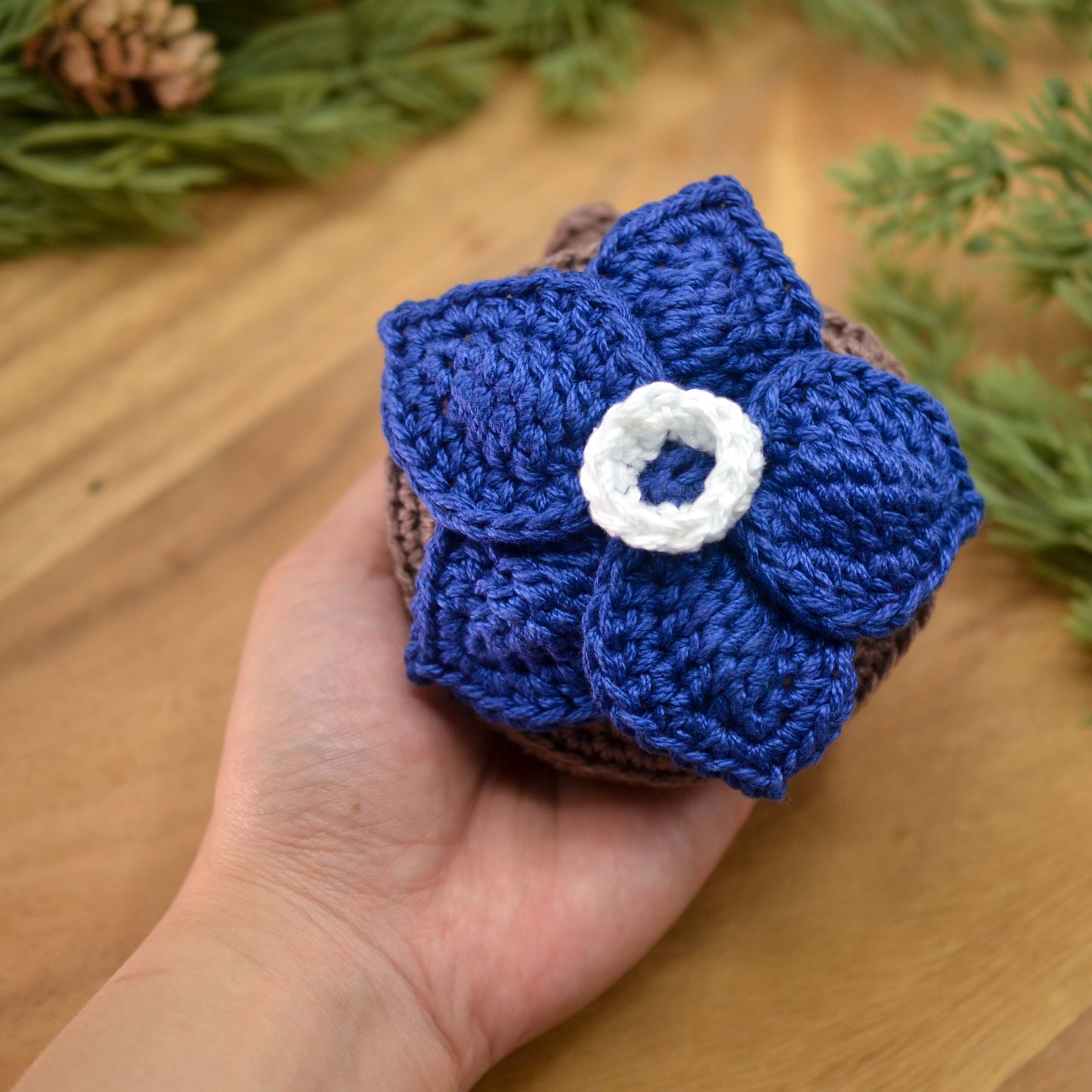 Hand holding a blue crocheted flower pouch with a white center on a wooden surface.