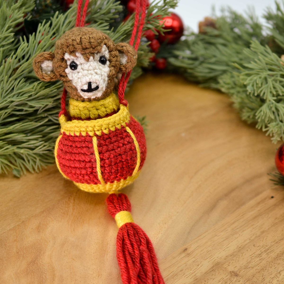 A crocheted monkey, wearing Lunar-New-Year clothing, is placed in a crocheted red lantern. The set is displayed on a wooden surface.