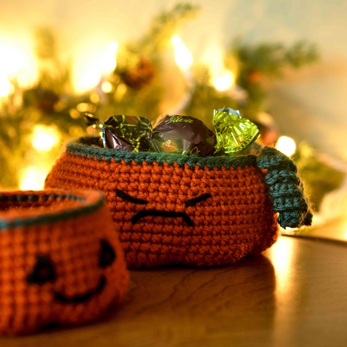 Two pumpkin bowls, made by following a crochet pattern, are used as candy dishes. The larger one in the back is currently holding wrapped chocolates.
