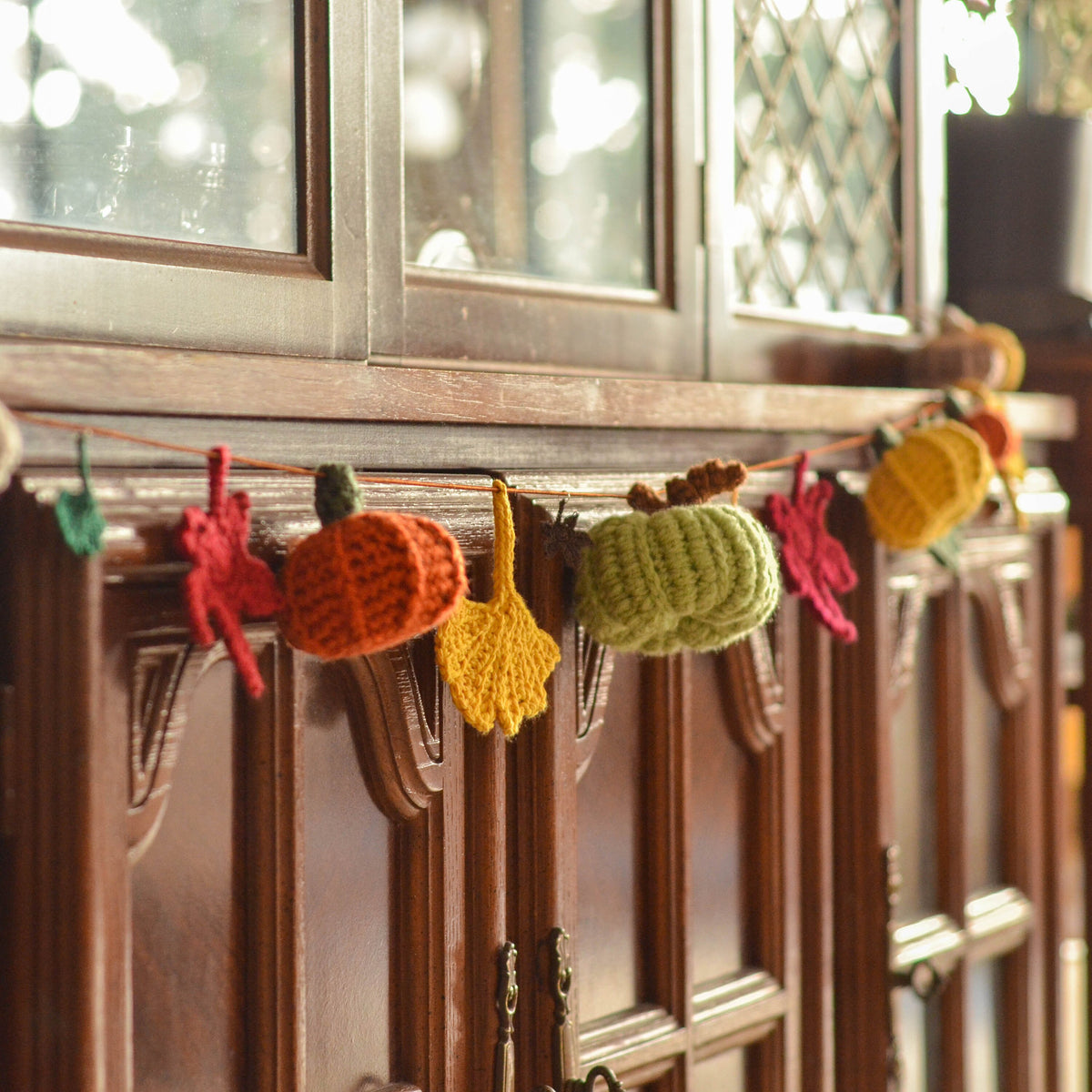 An crocheted autumn garland featuring pumpkins, ginkgo, and maple leaves. 