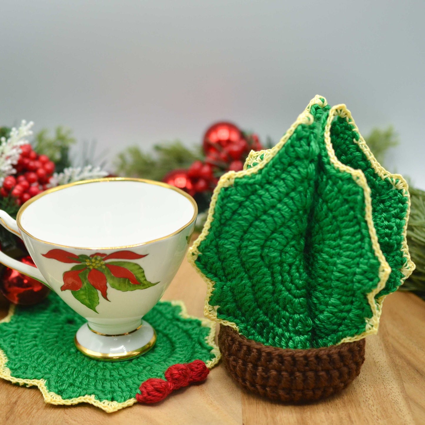 A holiday themed cup is placed on a holly leaf coaster. The rest of the coasters are stored in a dark-brown holder. The set looks like a Christmas tree. 