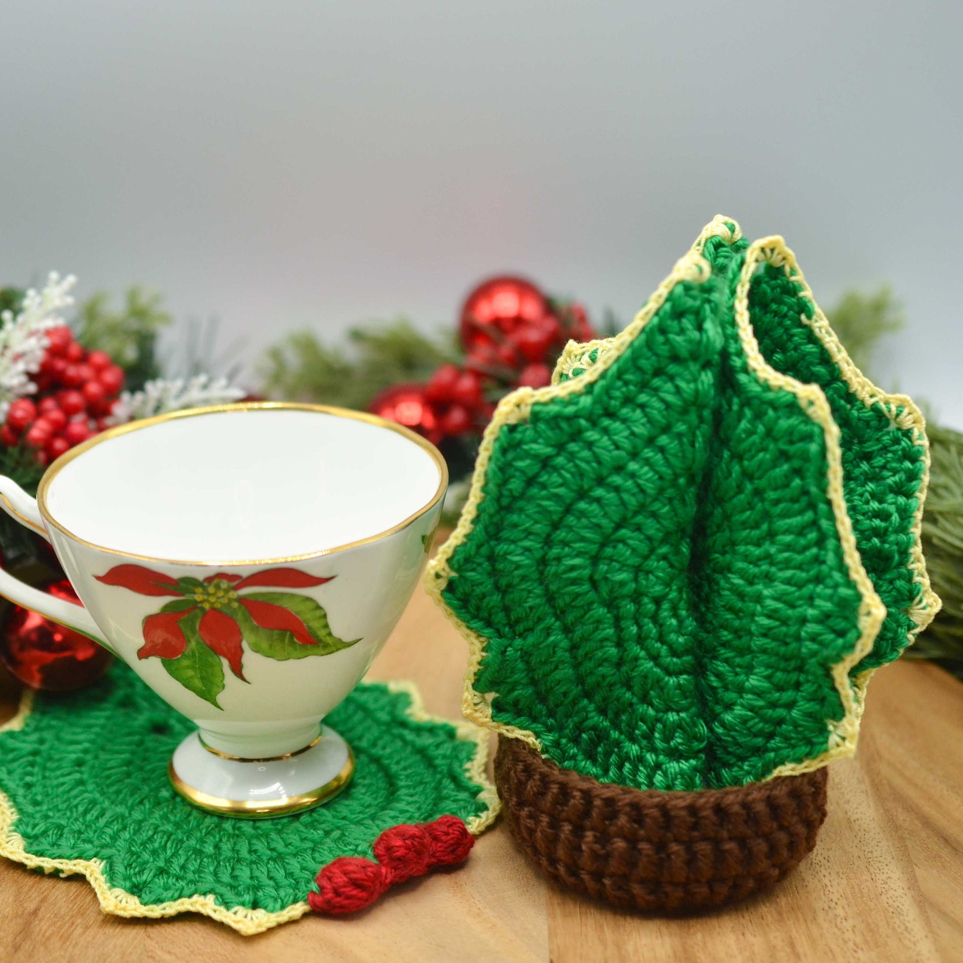 A holiday themed cup is placed on a holly leaf coaster. The rest of the coasters are stored in a dark-brown holder. The set looks like a Christmas tree. 