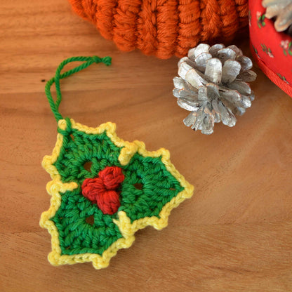 A holly leaf hanging ornament laying on the table. 