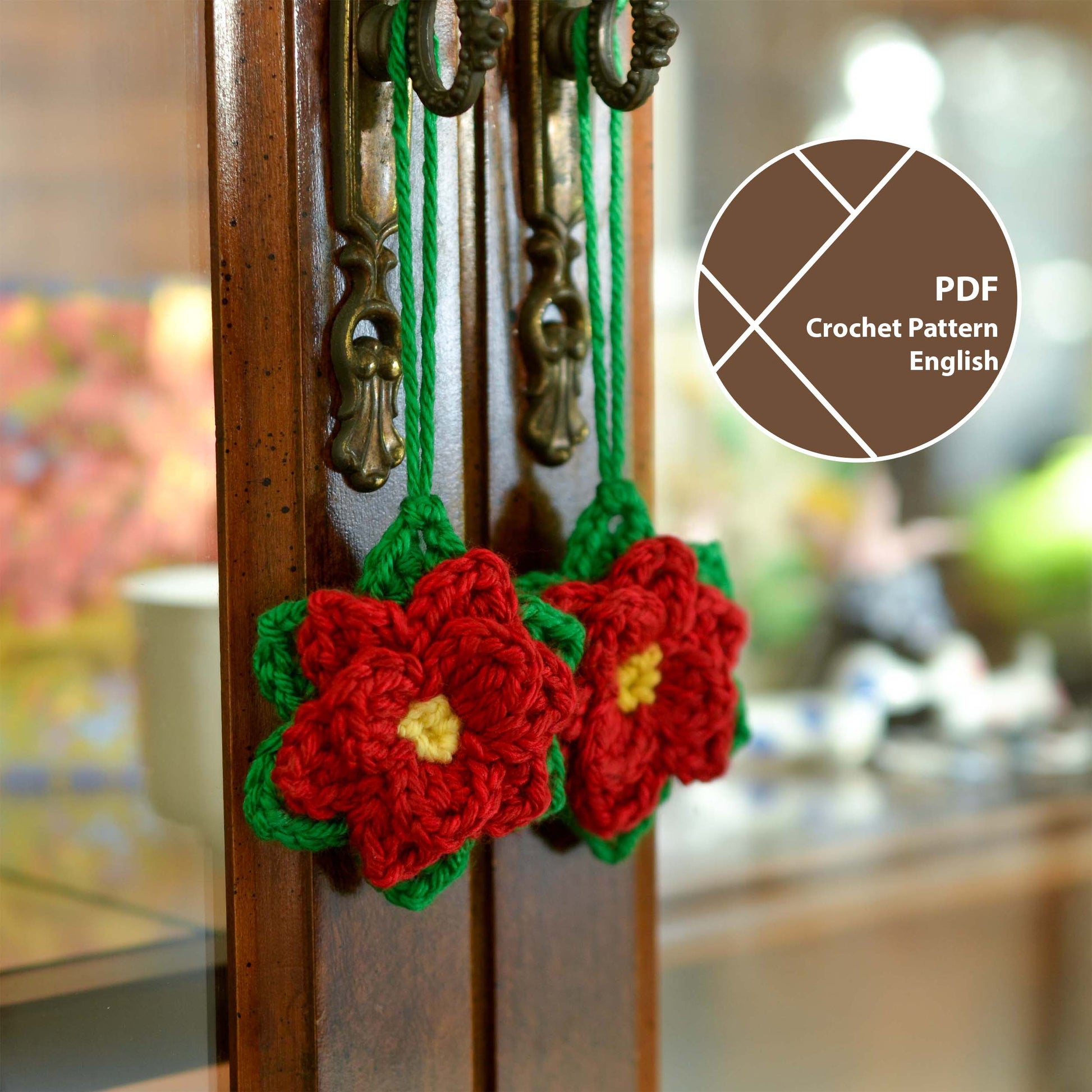 Two crocheted poinsettia ornaments. Each ornament is red with yellow centers and green leaves. They hang from antique-looking dark brown cabinet door knobs.