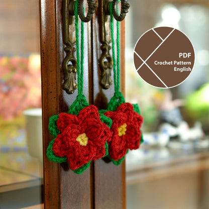 Two crocheted poinsettia ornaments. Each ornament is red with yellow centers and green leaves. They hang from antique-looking dark brown cabinet door knobs.