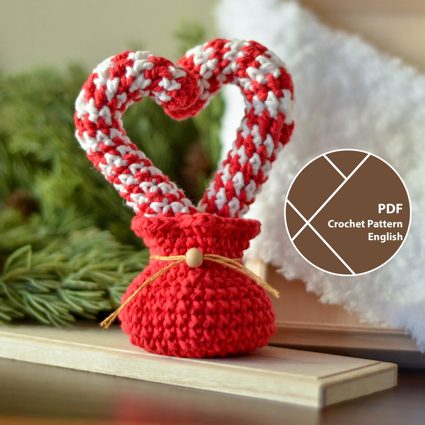 Two crochet candy canes formed a heart shape. There is a red crocheted holiday pouch at the bottom. The candy canes are in white and red. The red pouch has a gold ribbon and a wooden bead.