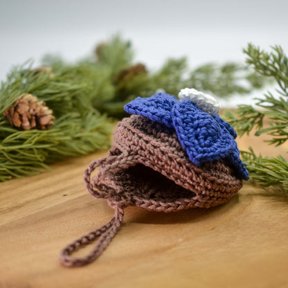 Crocheted floral pouch lying on the desktop against a greenery background. The pouch is half open, and it's empty. 