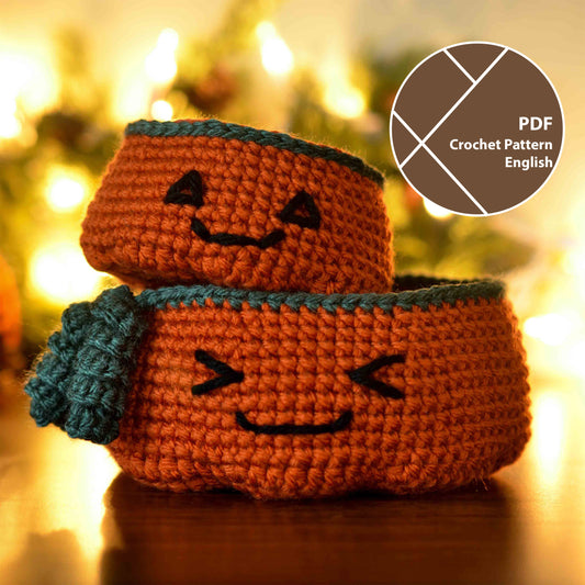 Two crocheted pumpkin-shaped baskets. The larger basket is larger and has a smiling face. The smaller basket has a Halloween-themed face. The smaller one is stacked on the top of the larger one. 