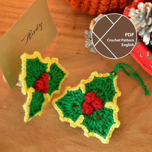 Crochet pattern for holly leaf ornaments. Two green and yellow holly leaf ornaments with red berries. The ornaments are small and would be suitable for Christmas tree decorations or other holiday crafts.  The image shows the finished crochet ornaments and a place card with the name 'Andy' written on it.
