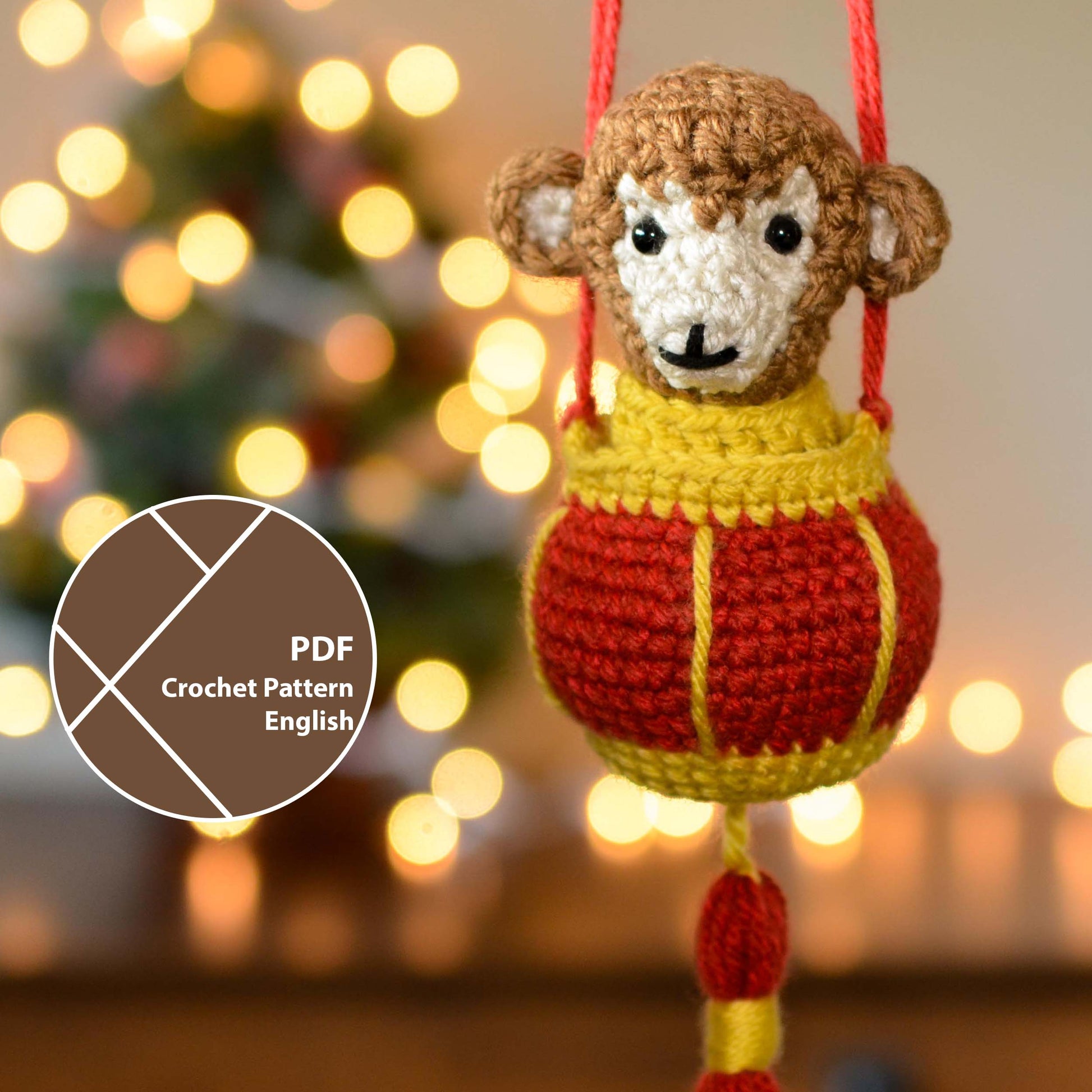 A crocheted monkey in a red lantern. The hanging ornament is displayed in front of a festive background. A label on the lower left corner indicates that this listing is a crochet pattern PDF that is written in English. 
