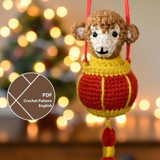 A crocheted monkey in a red lantern. The hanging ornament is displayed in front of a festive background. A label on the lower left corner indicates that this listing is a crochet pattern PDF that is written in English. 