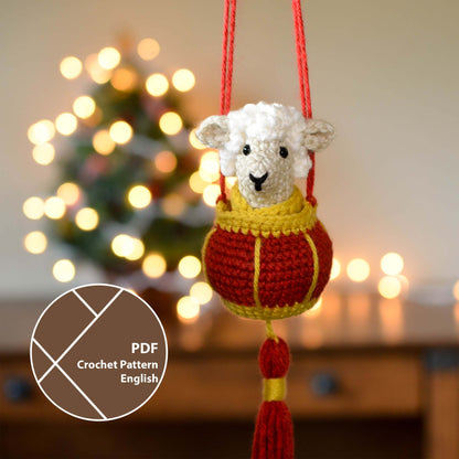 A crocheted sheep sitting in a red lantern basket. The set is a hanging ornament that is currently hanging in front of a festive background.