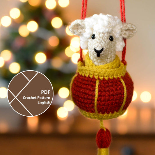 A crocheted sheep sitting in a red lantern basket. The set is a hanging ornament that is currently hanging in front of a festive background.