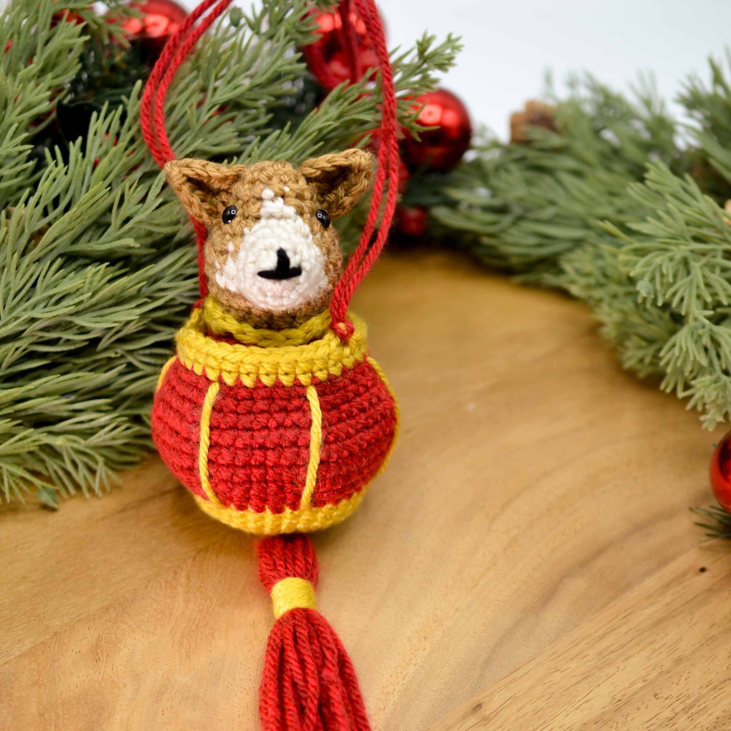 A crocheted dog placed in a red lantern. The set, displayed on a wooden surface, is an ornament for celebrating Lunar New Year.