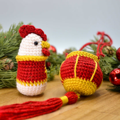 crocheted rooster and red lantern on a wooden surface; the rooster is facing right.