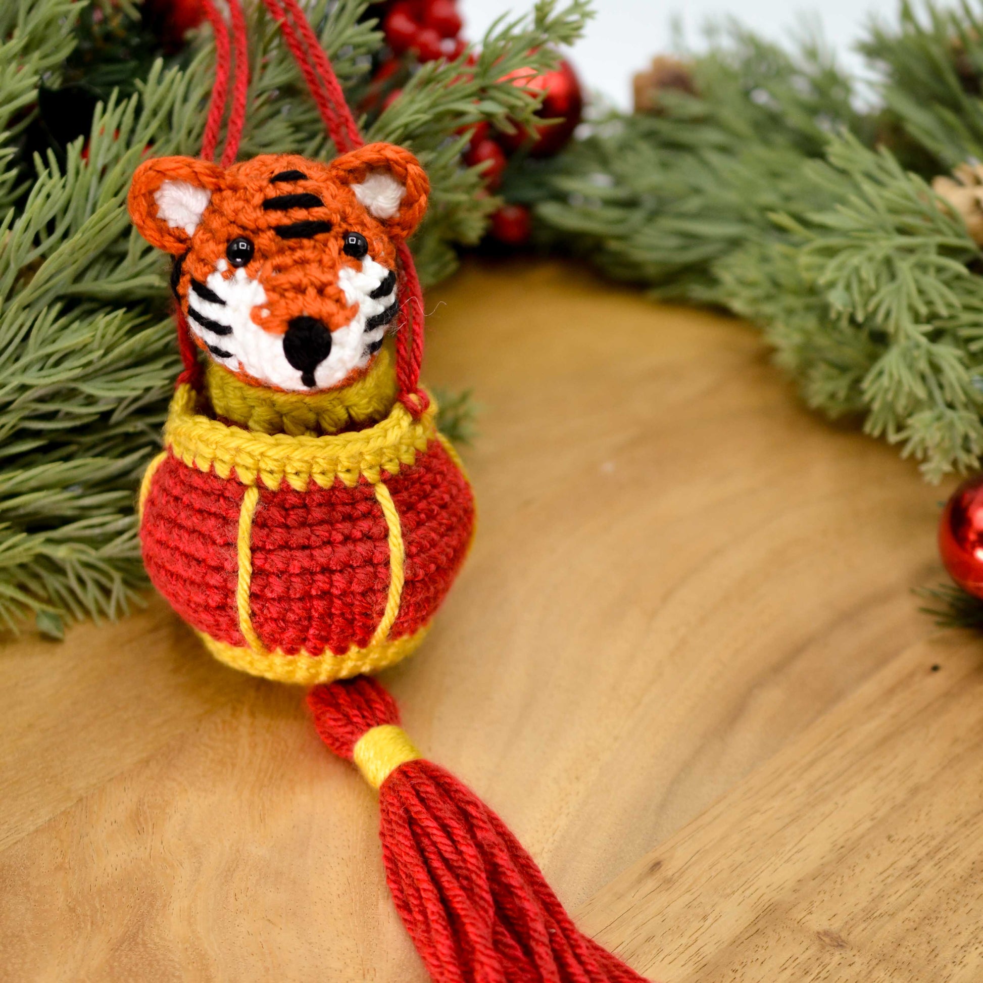 A crocheted lunar new year tiger is in a red lantern. The set is an ornament, placed on a wooden surface. 