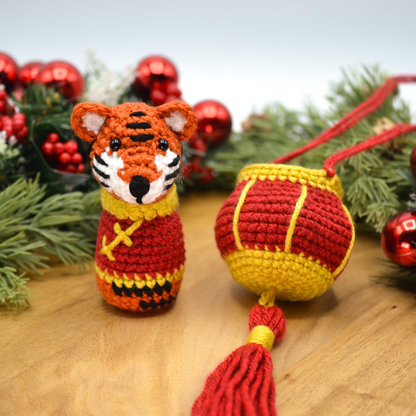 Crocheted tiger ornament and red lantern with tassel on a wooden surface with festive decorations in the background.
