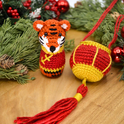 Crocheted tiger with a red lantern on a wooden surface with festive decorations.