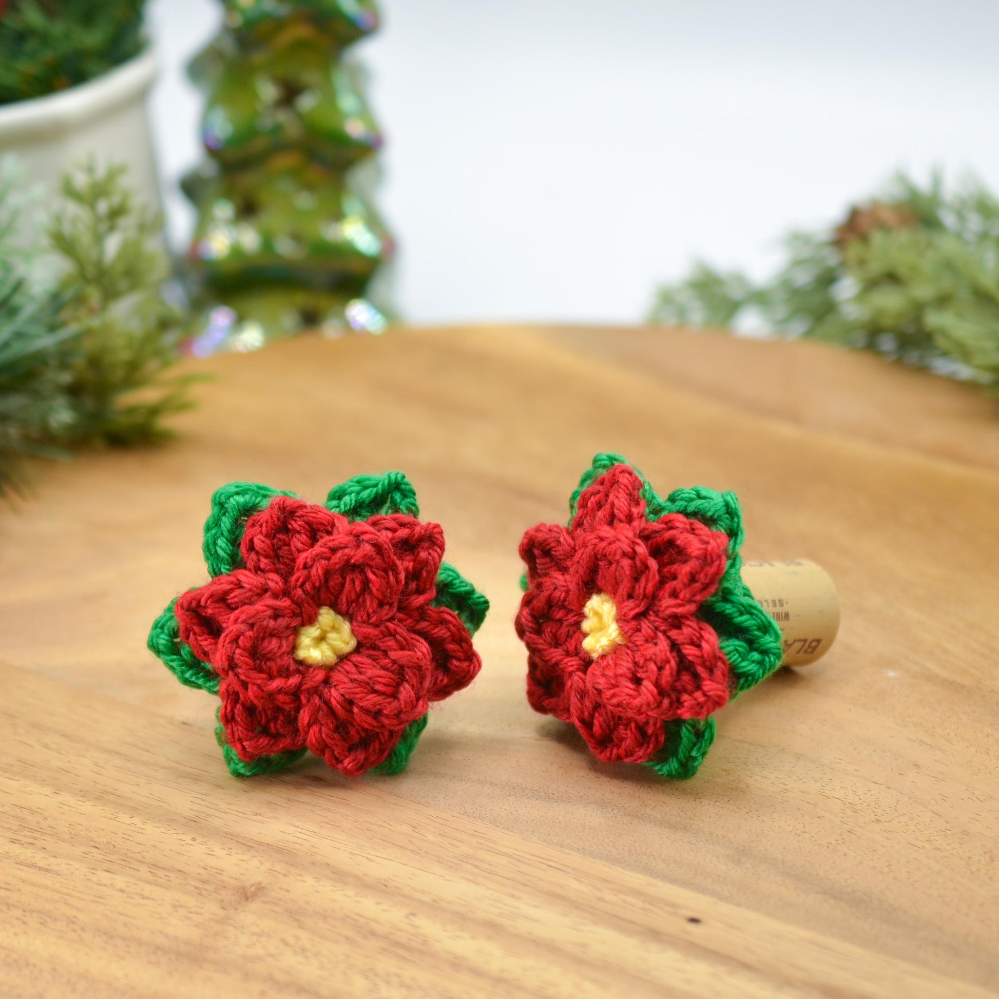 Two crocheted red poinsettia with yellow center and green leaves, attached to a wine cork.  The crocheted flowers are detailed and festive, perfect for Christmas decor or holiday gifts.