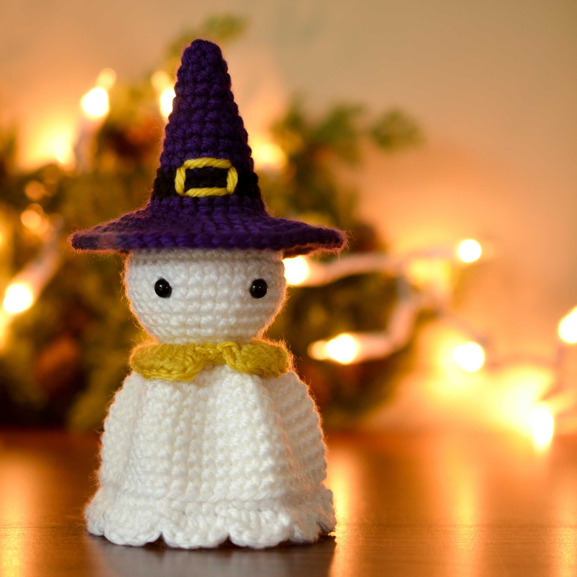The result of following a Halloween ghost crochet pattern: a cute ghost amigurumi wearing a purple witch's hat. 