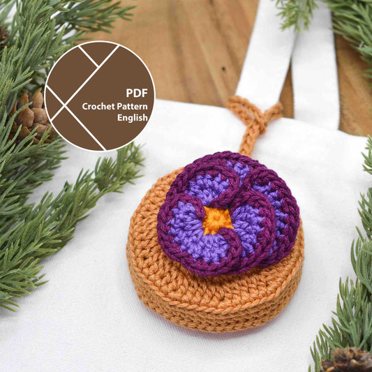 A crocheted pouch with a violet flower on the top. The pouch also doubles as a bag charm, hanging on a white tote canvas bag. 